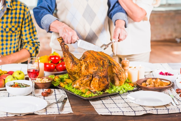 Corte humano de pollo asado en bandeja cerca de personas