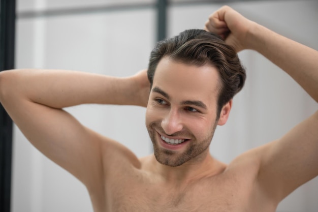 Cortes de cabello. Hombre guapo joven cepillándose el pelo y mirando contento