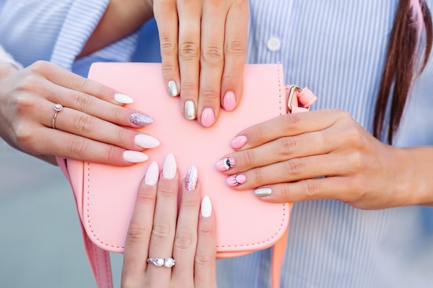 Cosecha de bolso rosa de cuero de moda sosteniendo dos manos de chicas con manicura de diseño mostrando en la cámara Manos femeninas con elegantes anillos de plata Concepto de moda de manicura y accesorios