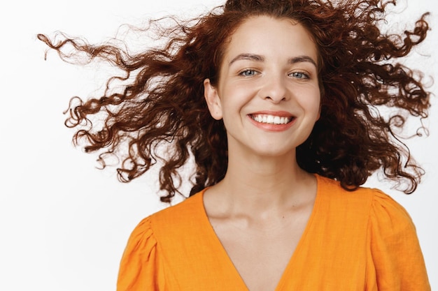 Cosméticos para el cuidado de la piel y el cabello. Hermosa mujer sonriente con cabello rojo rizado volando en el aire, flotando, sonriendo con dientes blancos y expresión de cara feliz, fondo de estudio