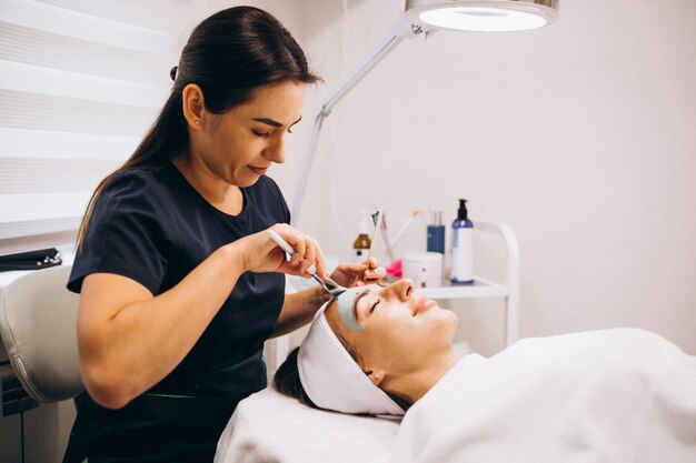 Cosmetóloga aplicando una máscara en la cara del cliente en un salón de belleza