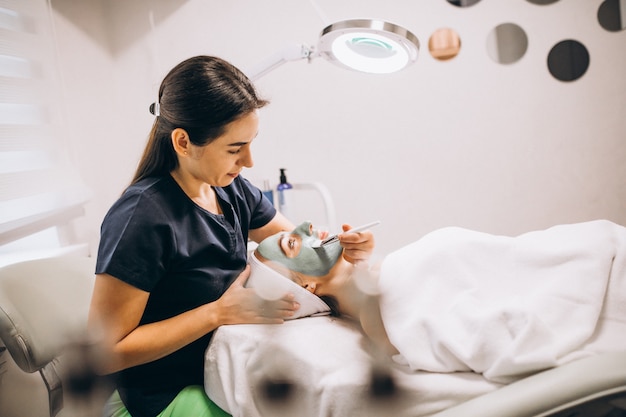 Cosmetóloga aplicando una máscara en la cara del cliente en un salón de belleza