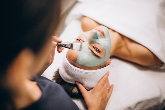 Cosmetóloga aplicando una máscara en la cara del cliente en un salón de belleza