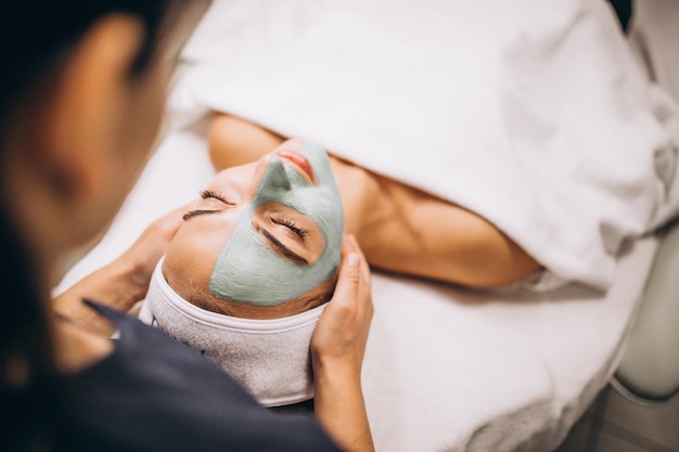 Cosmetóloga aplicando una máscara en la cara del cliente en un salón de belleza