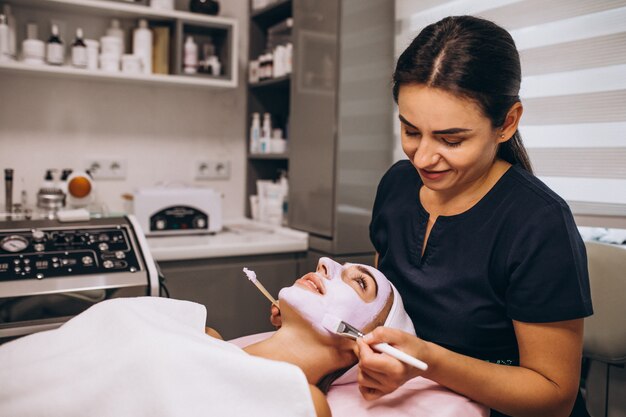 Cosmetóloga aplicando una máscara en la cara del cliente en un salón de belleza