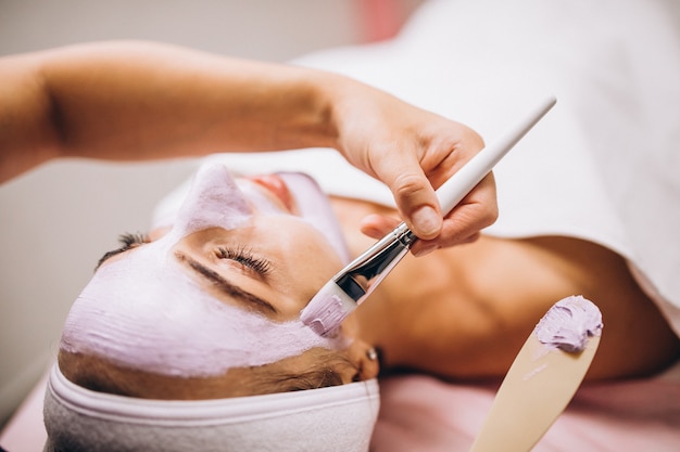 Cosmetóloga aplicando una máscara en la cara del cliente en un salón de belleza