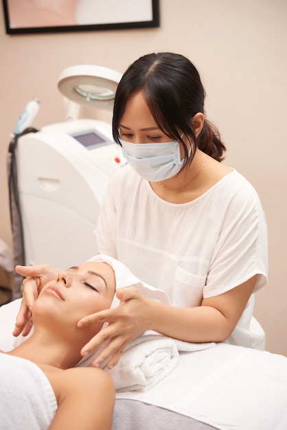 Cosmetólogo asiático dando masaje facial al cliente caucásico