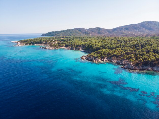 Costa del mar Egeo con agua azul transparente, vegetación alrededor, rocas, arbustos y árboles, vista desde el zumbido, Grecia