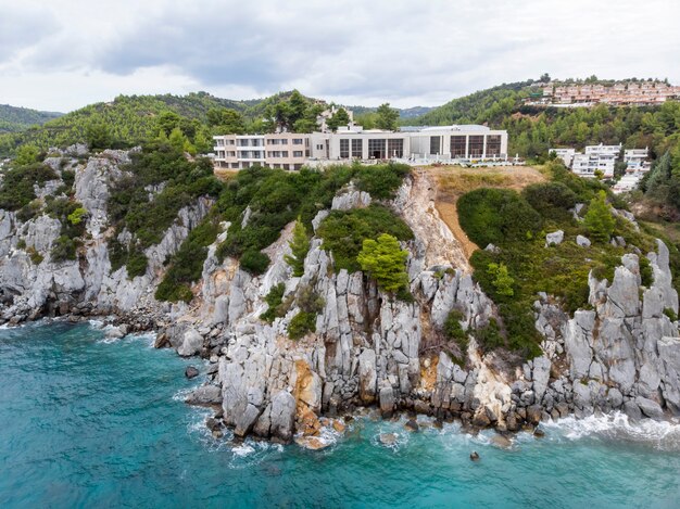 Costa del mar Egeo de Grecia, edificios de Loutra ubicados cerca de los acantilados rocosos, vegetación y agua azul. Vista desde el dron