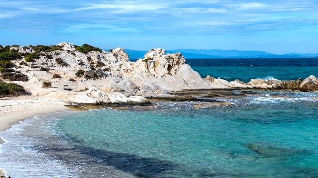 Costa del mar Egeo con vegetación alrededor, rocas y arbustos, agua azul con olas, Grecia