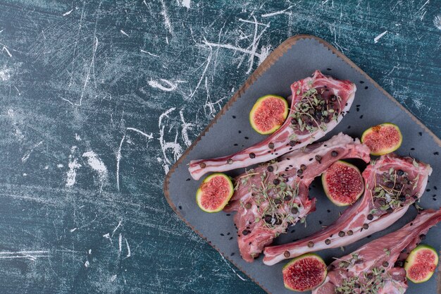 Costillas crudas en tablero de madera con higos y hierbas secas.