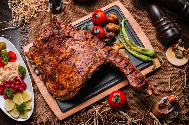 Costillas a la parrilla sobre la plancha de madera tomate pimiento patata vista superior