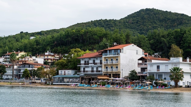 Costo del mar Egeo, sombrillas y tumbonas en la playa, edificios en la fila