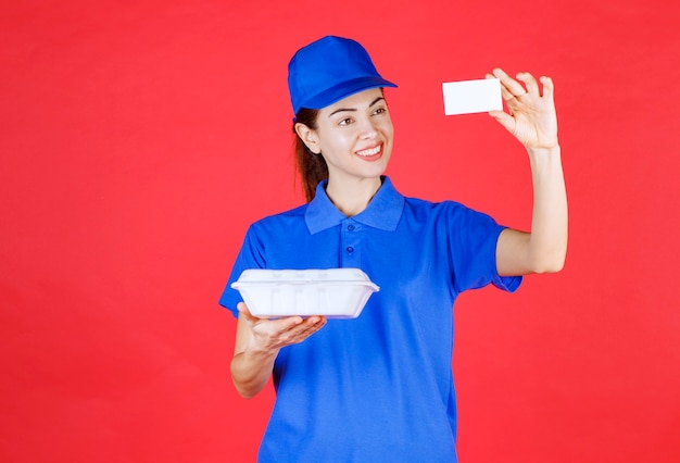 Courier Mujer sosteniendo una caja de comida para llevar blanca y presentando su tarjeta de visita.