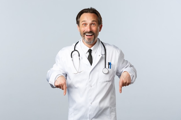 Covid-19, brote de coronavirus, trabajadores de la salud y concepto de pandemia. Feliz sonriente médico masculino en bata blanca que invita a hacer clic en el enlace. Terapeuta mostrando camino a la publicidad, invitando a pacientes