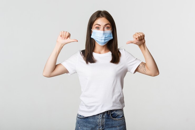 Foto gratuito covid-19, concepto de salud y distanciamiento social. atractiva mujer sonriente en máscara médica apuntando a sí misma, blanco.