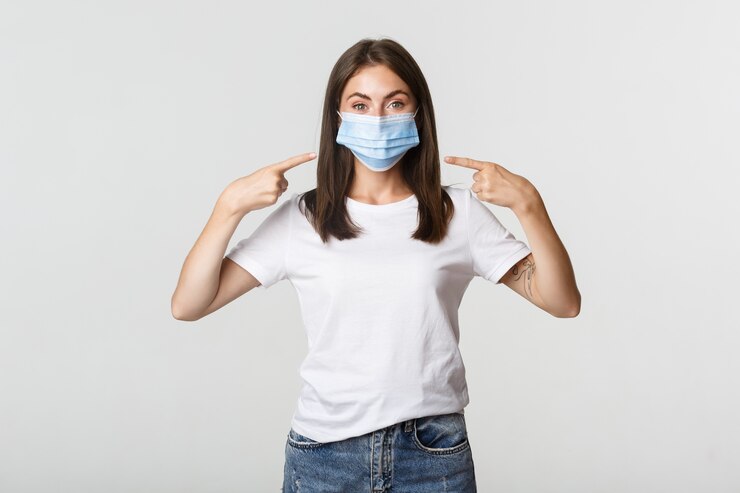 Foto gratuito covid-19, concepto de salud y distanciamiento social. chica morena atractiva en máscara médica que señala el dedo en la cara, blanco.