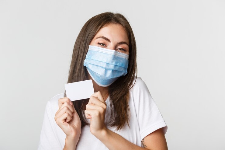 Foto gratuito covid-19, concepto de salud y distanciamiento social. primer plano de la atractiva chica morena feliz en máscara médica mostrando tarjeta de crédito.