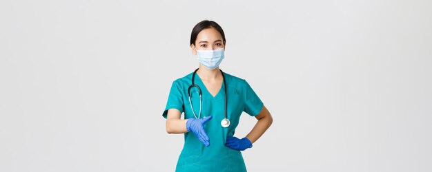 Covid-19, enfermedad por coronavirus, concepto de trabajadores de la salud. Confiada joven doctora asiática, médica con exfoliantes y máscara médica, guantes, extender la mano para apretón de manos, saludar al paciente