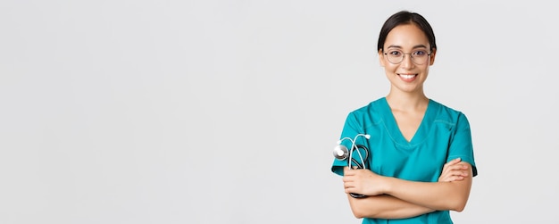 Covid-19, enfermedad por coronavirus, concepto de trabajadores de la salud. primer plano de confía en la doctora profesional, enfermera con gafas y matorrales de pie fondo blanco, brazos cruzados.