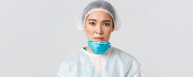 Covid-19, enfermedad por coronavirus, concepto de trabajadores de la salud. Primer plano de una doctora asiática cansada y exhausta que se quita el respirador y las gafas protectoras, la enfermera tiene daños en la piel después del turno en el hospital
