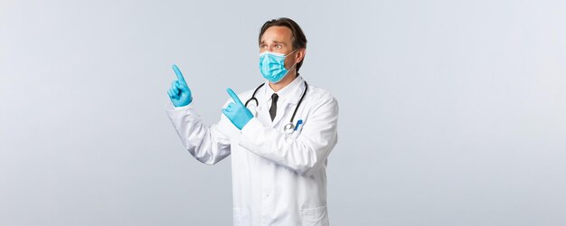 Covid-19, prevención de virus, trabajadores sanitarios y concepto de vacunación. Doctor de sexo masculino molesto y preocupado con máscara médica y guantes con aspecto ansioso, pánico apuntando hacia la esquina superior izquierda, mirando la pancarta