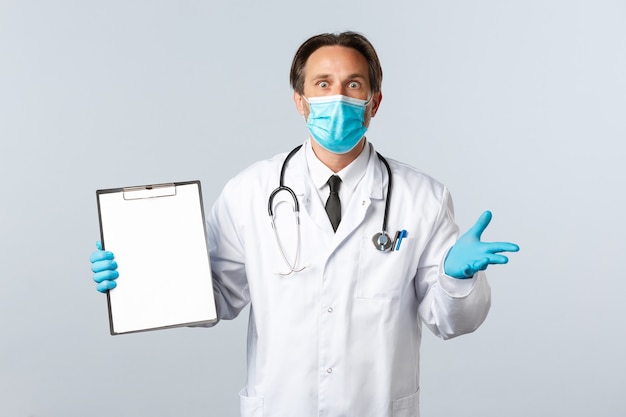 Covid-19, prevención de virus, trabajadores sanitarios y concepto de vacunación. Doctor de sexo masculino sorprendido y preocupado en máscara médica y guantes, mostrando los resultados de la prueba en el portapapeles