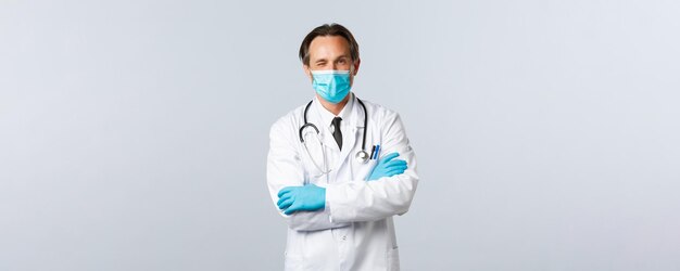 Covid-19, prevención de virus, trabajadores sanitarios y concepto de vacunación. Médico profesional amable con máscara médica y guantes, alienta al paciente a relajarse, todo bien, guiñando un ojo y cruzando los brazos en el pecho.