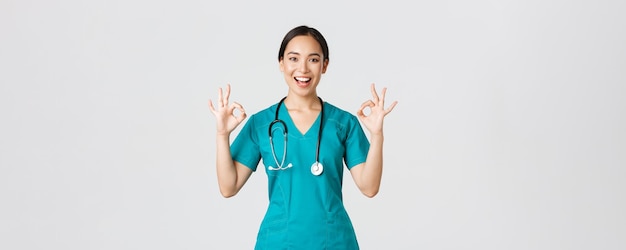 Covid-19, trabajadores de la salud, concepto de pandemia. Una doctora asiática profesional y segura de sí misma, pasante en matorrales asegura a los pacientes que todo está bien, mostrando un buen gesto satisfecho, sonriendo complacido.