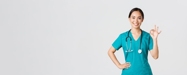Covid-19, trabajadores de la salud, concepto de pandemia. Una doctora asiática sonriente, profesional y segura de sí misma, una enfermera con matorrales asegura que todo esté bajo control, mostrando un buen gesto complacido.
