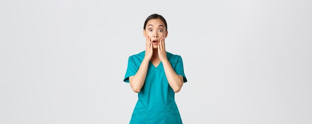 Covid-19, trabajadores de la salud, concepto de pandemia. Enfermera asiática sorprendida y asustada, doctor en matorrales mira la cámara sin palabras, jadeando asombrado, escucha el anuncio, quedando impresionado.