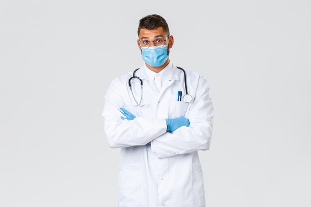 Covid-19, trabajadores de la salud, concepto de pandemia y prevención de virus. Sorprendido médico hispano con máscara médica y matorrales levantan las cejas asombrado, escuchan un caso interesante en la clínica.