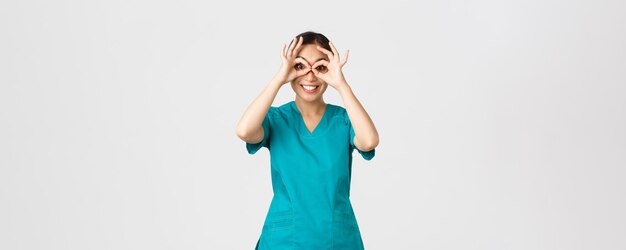 Covid-19, trabajadores de la salud y prevención del concepto de virus. Divertida, feliz, linda doctora asiática, pasante en matorrales mirando a través de binoculares de mano con expresión emocionada, sonriendo.