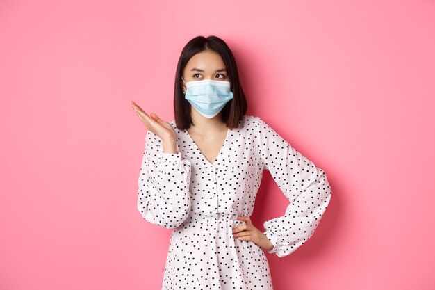 Covid concepto de cuarentena y estilo de vida hermosa mujer asiática en mascarilla levantando la mano de pie en dres ...