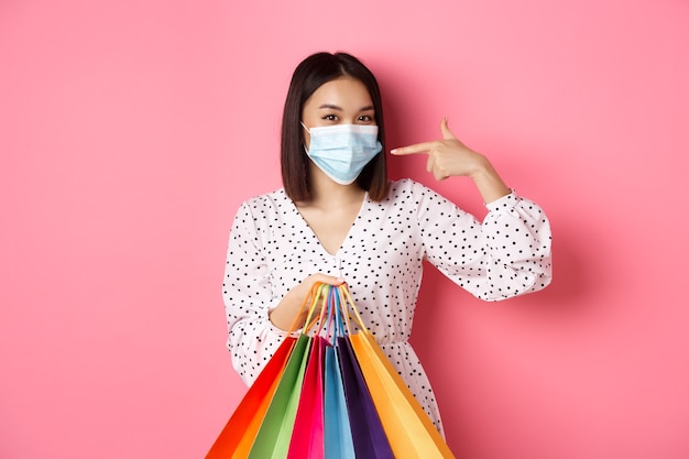 Covid pandemia y concepto de estilo de vida linda mujer asiática sosteniendo bolsas de compras sonriendo y apuntando a ...