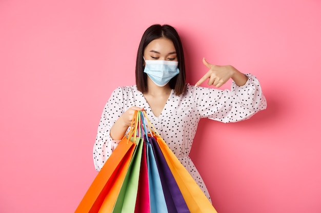 Covid pandemia y concepto de estilo de vida mujer bastante coreana en máscara médica apuntando a bolsas de la compra ...