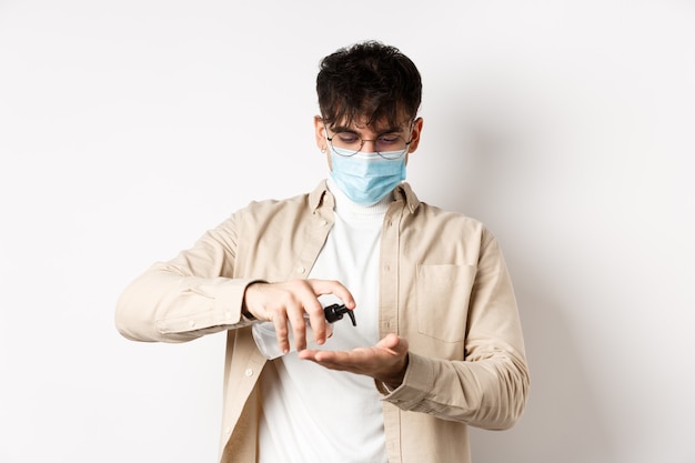 Covid salud y concepto de cuarentena joven hispano en gafas y mascarilla usando desinfectante de manos ...