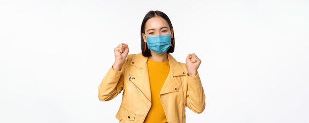 Covid19 y concepto de personas Joven asiática con mascarilla médica bailando feliz con ropa informal posando sobre fondo blanco