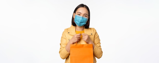Covid19 y concepto de tienda Joven mujer asiática elegante con mascarilla médica sosteniendo una bolsa de compras en los centros comerciales durante la pandemia de fondo blanco