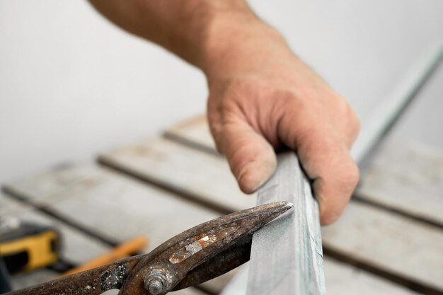 Craftsman corta perfiles de acero para paneles de yeso, primer plano, enfoque selectivo. Preparación para la instalación del marco del sistema de perfil de techo. Renovación y renovación
