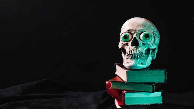 Cráneo espeluznante con ojos de lujo en la pila de libros
