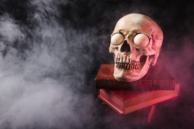 Cráneo espeluznante en la pila de libros en el humo