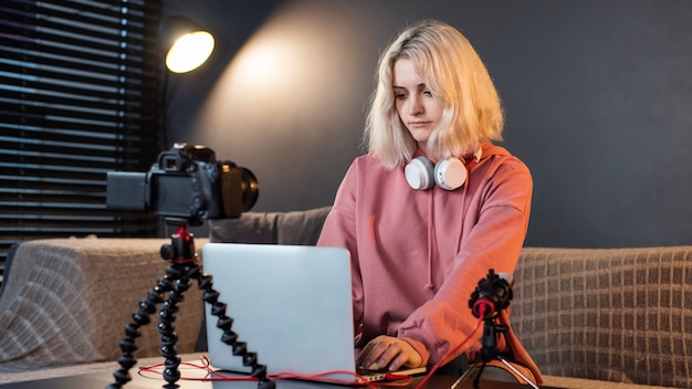 Creador de contenido joven chica rubia con auriculares trabajando en su computadora portátil en la mesa con cámara