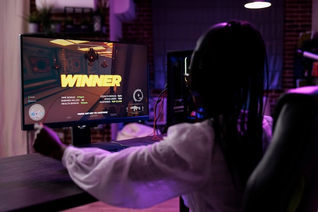 Creador de contenido jugando torneo de videojuegos en computadora, celebrando la victoria. Jugadora ganadora del campeonato de juegos de acción, divirtiéndose con la competencia de juegos en línea en la PC.