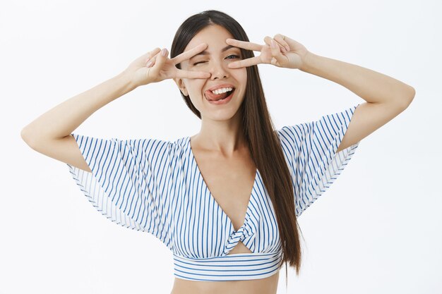 Creativa mujer asiática encantada y relajada en elegante top recortado sacando la lengua