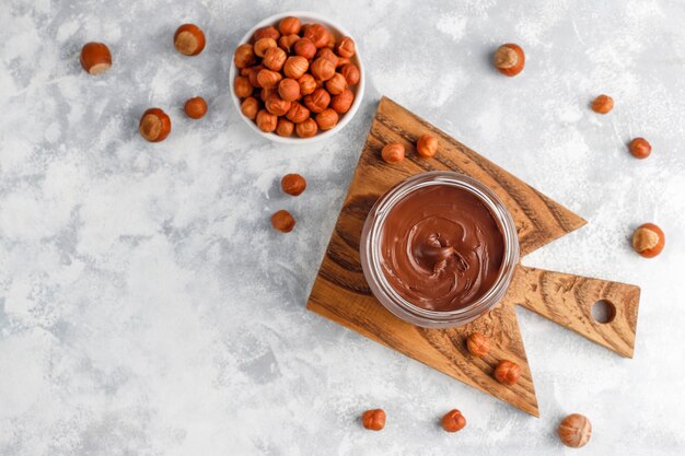 Crema de chocolate o turrón con avellanas en frasco de vidrio sobre hormigón, copyspace