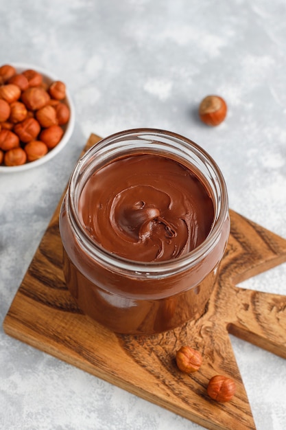 Crema de chocolate o turrón con avellanas en frasco de vidrio sobre hormigón, copyspace