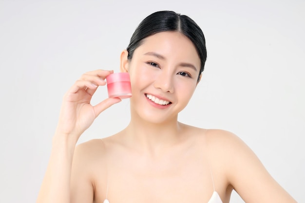 Crema facial cosmética Primer plano Cara de belleza Mujer asiática con piel limpia y fresca Sosteniendo una botella de crema facial aislada en blanco Concepto de belleza y cuidado de la piel