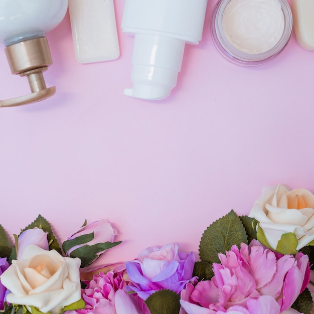 Crema hidratante y flores falsas sobre superficie rosa.