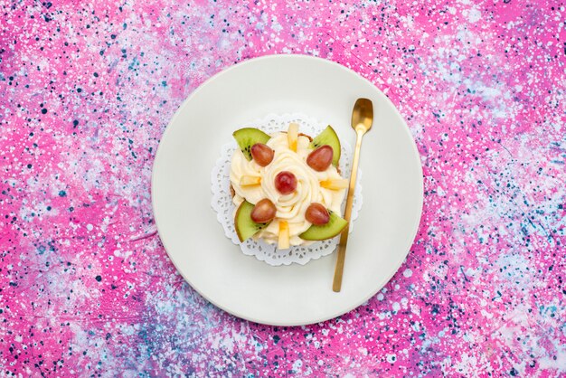 Crema de pastel de vista superior con frutas frescas en rodajas dentro de la placa en el color dulce de la galleta de la torta de fondo de color